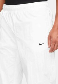 Vita sportshorts i lätt material, med elastisk midja och en svart Nike-logotyp på vänster sida.
