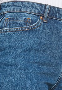 Blå denimjeans med orange sömmar, en liten ficka på baksidan och en mjuk yta. Tyget verkar något blekt på vissa ställen.