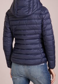 Námořnicky modrá prošívaná péřová bunda s kapucí, s horizontálním prošíváním, hladkou texturou a přiléhavým střihem. Doplněná modrými džínami.