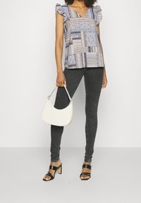 Top corto de manga corta con un patrón en azul, beige y marino. Combinado con jeans ajustados negros y sandalias de tacón negro con tiras. Sosteniendo un bolso blanco.