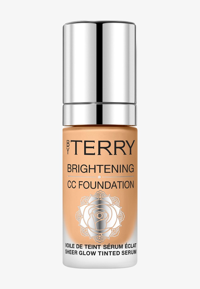 CC-Foundation in einer transparenten Glasflasche. Helles Orange mit fettem schwarzen Text und einem silbernen Deckel. Das Etikett zeigt ein Rosendesign.