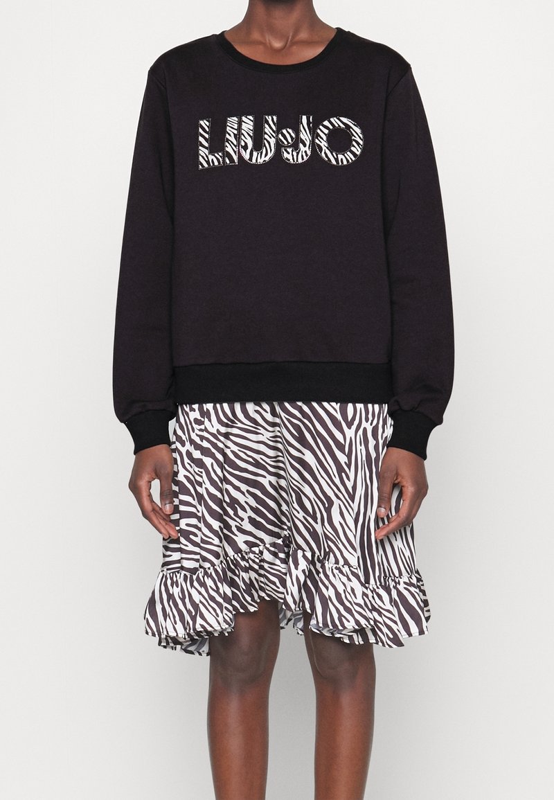 Sweatshirt noir avec le logo « LIU-JO », associé à une jupe à volants imprimé zèbre en blanc et brun. Tissu texturé, manches longues, poignets élastiques.