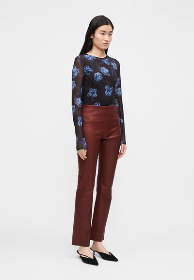 Long-sleeve black mesh top with blue floral print, paired with high-waisted burgundy leather pants. Model stands in a neutral background.