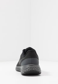 Zapatilla deportiva negra con parte superior de malla texturizada, cuello acolchado y suela gris esculpida con forma redondeada.