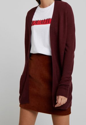 Burgundy ribbed cardigan with open front, paired with a white graphic tee featuring “EQUALITY” in red, and a rust-colored corduroy skirt.