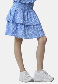 Gonna a strati con stampa floreale blu e vita smock, abbinata a sneakers bianche con sovrapposizioni in rete e texture.
