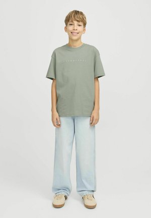 Gaiši zaļa kokvilnas T-kreklu ar baltu uzrakstu "JACK & JONES", apvienots ar gaiši ziliem platajiem biksēm un bēšām sporta apavām.