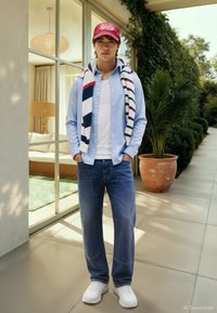 Blå skjorte over en hvit t-skjorte, blå jeans, hvite joggesko og en rød caps. Et stripete skjerf henger rundt halsen.