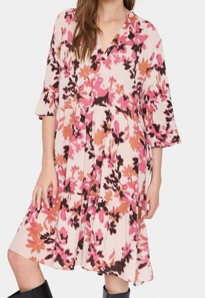 Vrouw draagt een bloemen midi-jurk met roze, oranje en zwarte patronen, driekwartmouwen en zwarte laarzen.