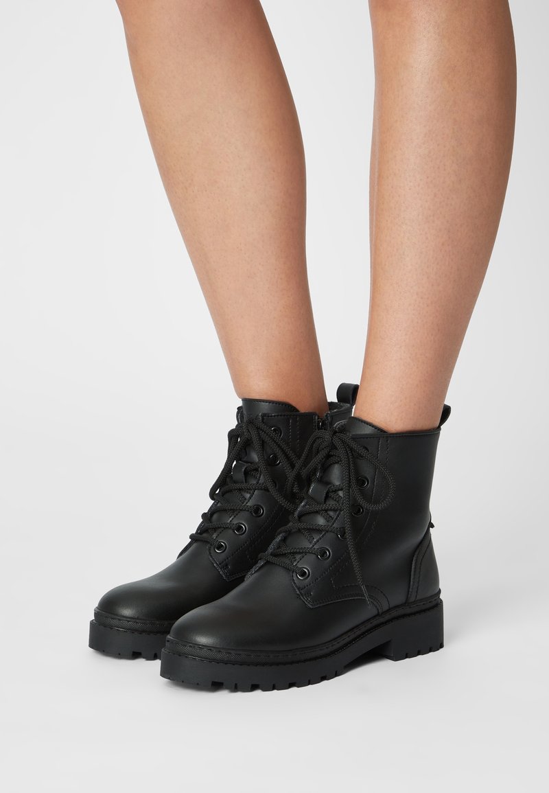 Botas de cuero negras hasta el tobillo con punta redonda, cordones en la parte delantera y suela robusta. Presentan detalles de costura y un colar acolchado para mayor comodidad.