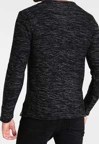 Pull en maille texturée noire et grise avec manches longues, col rond et coupe ajustée, vu de dos.