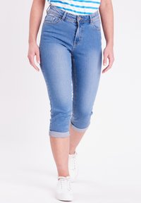 Vaqueros capri de mezclilla azul claro con puños enrollados, diseño de cinco bolsillos y cremallera. Combinados con zapatillas blancas. Textura suave.