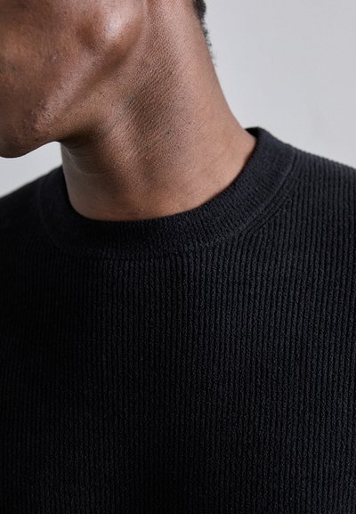 Zwarte ribbelgebreide trui met een ronde halslijn, die een textuurpatroon op de stof laat zien en een close-up van het kraaggebied.