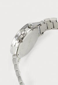 Montre en acier inoxydable argenté avec un boîtier rond, couronne et poussoirs visibles, et un bracelet en maillons métalliques. Dos gravé avec les détails de la marque.