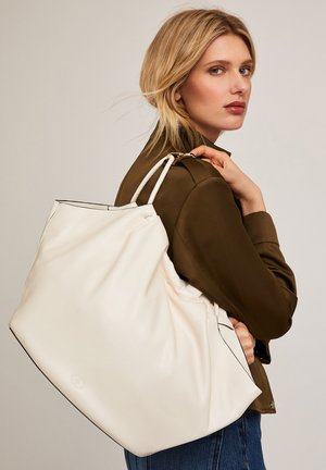 Große cremefarbene Tragetasche mit glatter Textur, die schwarze Kantenverarbeitung entlang der Ränder und doppelte Schulterriemen aufweist.