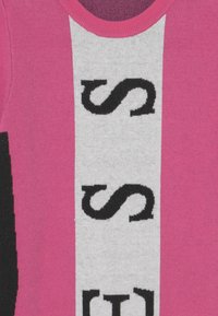 Maglione rosa con una grande fascia centrale bianca con testo nero, scollatura rotonda e pannelli laterali neri a contrasto.