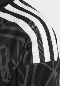 Schwarze Sportbekleidung mit geometrischem Muster, weißen und schwarzen Streifenakzenten sowie strukturiertem Mesh-Detailing an der Schulter.