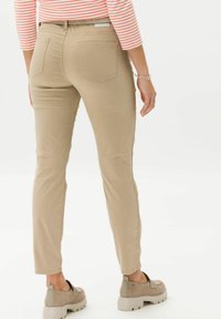 Beige slim-fit pants with a smooth texture, five-pocket design, and a mid-rise waistband. Worn with gray slip-on shoes.