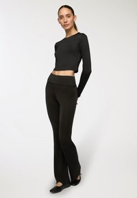 Top corto a maniche lunghe nero abbinato a pantaloni neri aderenti. Tessuto morbido, design a gamba svasata e scarpe piatte completano l'outfit.