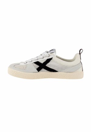 Zapatilla deportiva blanca de malla con suela beige, logo negro en forma de "X" en el lateral, cordones blancos y lengüeta negra en el talón.