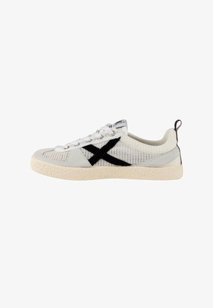 Zapatilla deportiva blanca de malla con suela beige, logo negro en forma de "X" en el lateral, cordones blancos y lengüeta negra en el talón.