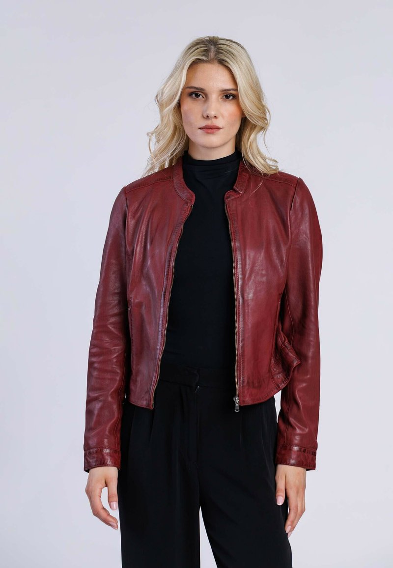 Veste en cuir rouge avec un col montant, fermeture éclair et coupe ajustée. Texture lisse et manches longues, associée à un haut noir.