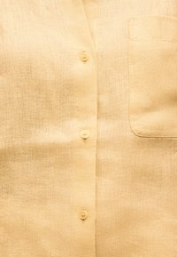 Μπεζ λινό πουκάμισο με εμπρόσθια τσέπη και τρία ορατά μπεζ κουμπιά κατά μήκος της κεντρικής λωρίδας.
