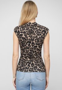 Top senza maniche con stampa leopardata e texture a coste, caratterizzato da un punto vita aderente e un motivo in nero e marrone. Abbinato a jeans azzurri chiari.