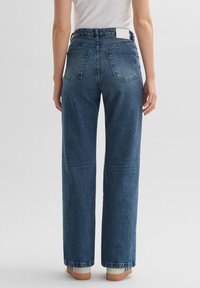 Jean bleu à taille haute et jambes larges avec une texture denim classique. Comprend deux poches arrière et une étiquette blanche à la taille.