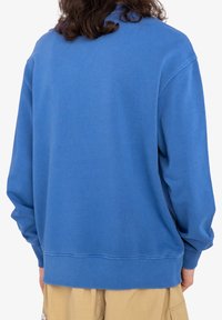 Sweat-shirt bleu avec une coupe décontractée, des poignets et un ourlet côtelés, et une texture douce. Aucun motif notable ou détail de quincaillerie visible.