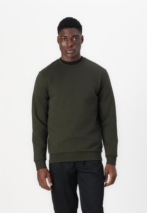 Olivegrüner Sweatshirt mit Rundhalsausschnitt und gerippten Bündchen, aus strukturiertem Stoff; kombiniert mit schwarzen Hosen, die ein nahtloses Design aufweisen.