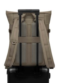 Brauner Rucksack mit doppelten Schultergurten, Netzpolsterung und einem oberen Griff, montiert auf einem schwarzen Koffer mit Rollen.