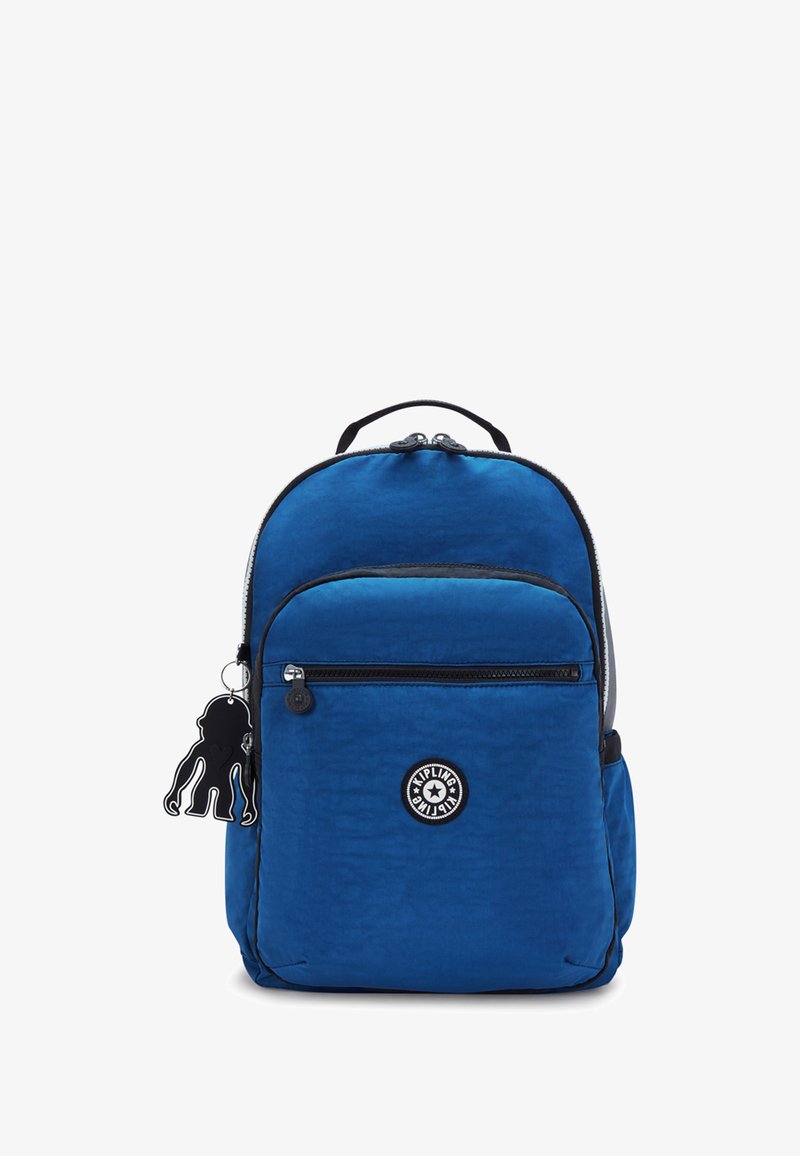 Zaino in nylon blu con tasca frontale con zip, manico superiore, spallacci regolabili e un ciondolo in plastica nera attaccato. Logo del marchio circolare al centro.