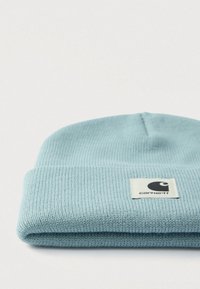 Μπλε πλεκτός σκούφος με διπλωμένο ρεβέρ και τετράγωνο έμβλημα με στυλιζαρισμένο γραφικό. Υφασμάτινη υφή, απαλή εμφάνιση και ζεστός σχεδιασμός.