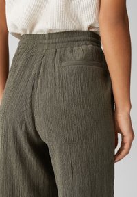 Olivově zelené plisované kalhoty s texturovaným povrchem, s nařaseným pasem a jednou zadní kapsou.