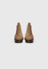Bottines en daim marron avec des panneaux élastiques sur les côtés, bout rond et petit talon empilé. Elles présentent une languette à l'arrière pour un enfilage facile.
