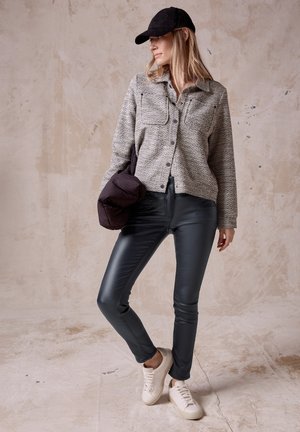 Ležérní outfit se skládá z texturované šedé košile na knoflíky, černých slim-fit kalhot a bílých tenisek, doplněný černou kšiltovkou a nadýchanou taškou.