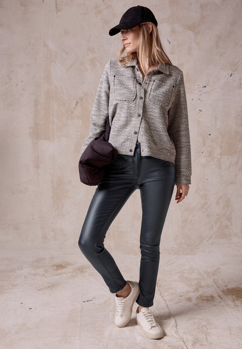 Avslappnad outfit med en strukturerad grå skjorta med knappar, svarta slim-fit byxor och vita sneakers, kompletterad med en svart keps och en puffig väska.