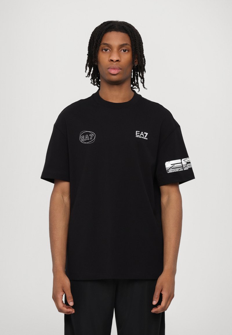 Black cotton t-shirt with a round neckline. Features EA7 logo on the chest and a graphic design on the left sleeve. Loose fit.