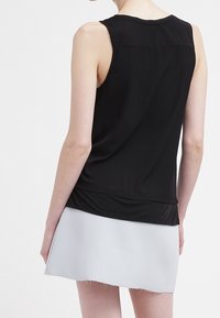 Svart ärmlös topp i slät textil, med rundad krage och något längre bakstycke, tillsammans med en ljusgrå minijurk.