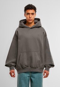 Hoodie grigio oversize con tasca frontale, polsini a coste e un grande cappuccio. Presenta un marchio discreto sul petto e maniche a motivo.