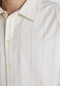 Camicia bianca con sottili righe verticali, colletto abbottonato e ricamo "Lyle & Scott" in beige, in tessuto di cotone con una trama morbida.