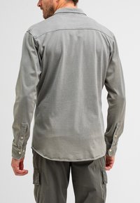 Grijze lange mouw shirt met een button-down kraag, met een zachte textuur en een gebogen zoom. Knopen op de manchetten voegen detail toe.