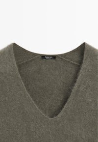 V-Ausschnitt Pullover aus weichem, grünlich-grauem Wollmix. Hat eine strukturierte, flauschige Oberfläche mit einem subtilen Glanz. Etikett ist am Ausschnitt sichtbar.
