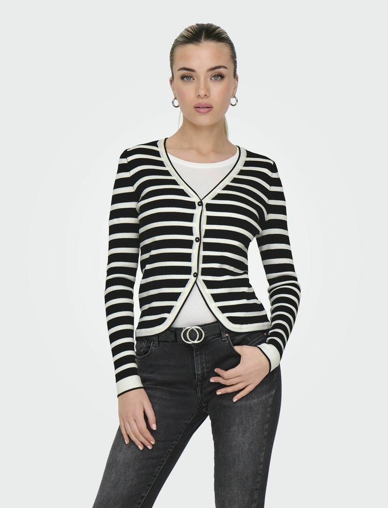 Gestreifter Cardigan in Schwarz und Weiß mit taillierter Passform, V-Ausschnitt, Knopfverschluss und gerippten Bündchen, kombiniert mit dunklen Jeans und einem Gürtel.