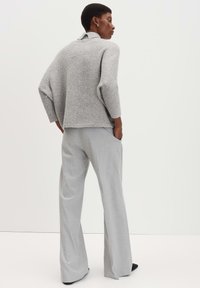 Grauer, locker sitzender Pullover mit hohem Kragen und weiten Ärmeln, kombiniert mit hellgrauen, weiten Hosen aus einem weichen Stoff.