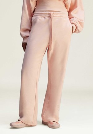 Light pink sweatpants made of soft fabric, featuring wide legs, an elastic waistband with drawstring, and a subtle logo near the hem.