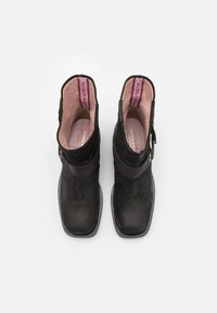 Bottines noires en cuir velours, avec une large sangle, un bout rond et une doublure rose pâle à l'intérieur.