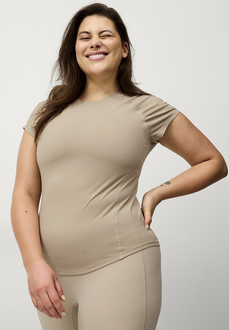 Beige tætsiddende træningsbluse med korte ærmer, sømløs design, glat tekstur og diskret side-rynkning, parret med matchende leggings.