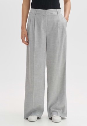 Femme portant un pantalon large gris clair avec des plis, des poches latérales, associé à des baskets blanches et un haut noir sans manches.